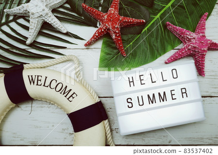 Hello Summer text in light box with green leave, starfish and lifebuoy decoration on wooden background Hello Summer text in light box with green leave, starfish and lifebuoy decoration on wooden background 83537402