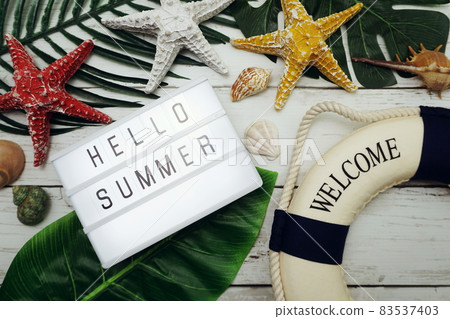 Hello Summer text in light box with green leave, starfish and lifebuoy decoration on wooden background Hello Summer text in light box with green leave, starfish and lifebuoy decoration on wooden background 83537403