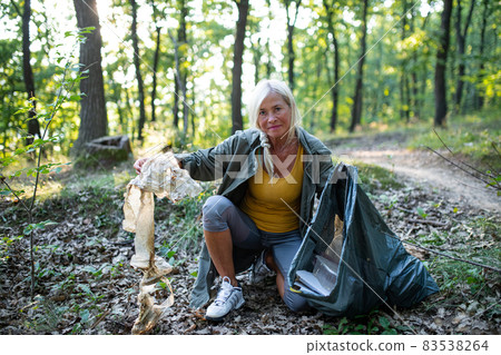 Senior woman ecologist picking up waste outdoors in forest. 83538264