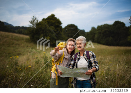 Happy mid adult woman with active senior mother hiking and looking at map outdoors in nature. 83538289