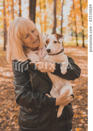 Senior smiling woman hugging her dog in autumn park. Active aging and pet concept. 83538884