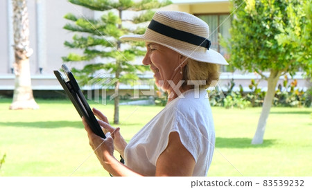 Senior female blonde businesswoman in hat uses tablet pc, digital tablet for business work or study Senior female blonde businesswoman in hat uses tablet pc, digital tablet for business work or study 83539232