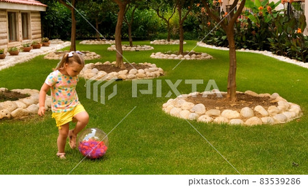 cheerful cute little girl, 3 years old, with two ponytails on her head, wearing a multi-colored T 83539286