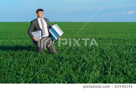 businessman poses in a green field, he goes with the documents and ladder, freelance and business concept, green grass and blue sky as background businessman poses in a green field, he goes with the documents and ladder, freelance and business concept, green grass and blue sky as background 83540141
