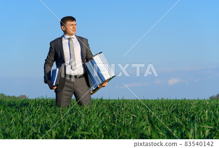 businessman poses in a green field, he goes with the documents and ladder, freelance and business concept, green grass and blue sky as background 83540142