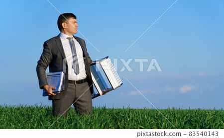 businessman poses in a green field, he goes with the documents and ladder, freelance and business concept, green grass and blue sky as background 83540143