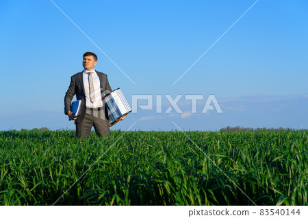 businessman poses in a green field, he goes with the documents and ladder, freelance and business concept, green grass and blue sky as background 83540144
