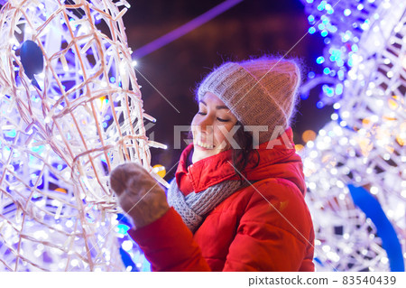 Winter holiday season. Christmas, New Year concept. Funny happy woman spend time having fun near illuminated and decorated showcase on city street. 83540439