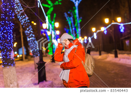 Winter holiday season. Christmas, New Year concept. Funny happy woman spend time having fun near illuminated and decorated showcase on city street. 83540443