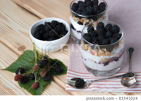Blackberry berries in a summer dessert - cheesecake in glasses on a wooden background. Healthy snack 83541024