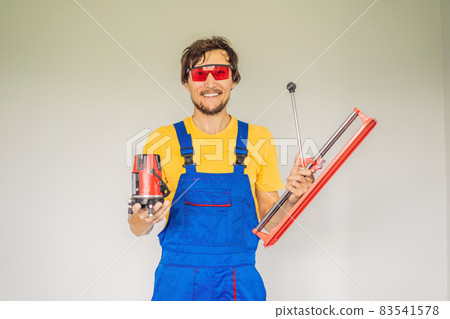 A tiler, a tiling specialist, holds a tile cutter in his hands A tiler, a tiling specialist, holds a tile cutter in his hands 83541578