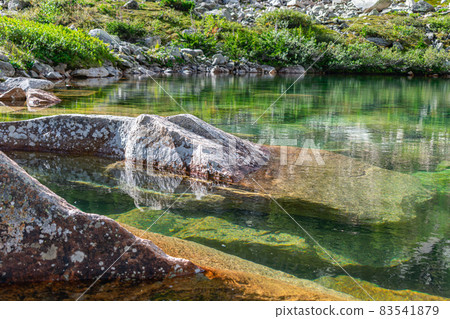 A clean green lake from which huge granite stones stick out A clean green lake from which huge granite stones stick out 83541879