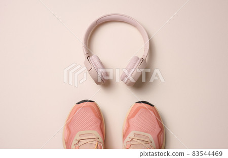 pair of pink textile sneakers, wireless headphones on a beige background. Set for sports pair of pink textile sneakers, wireless headphones on a beige background. Set for sports 83544469