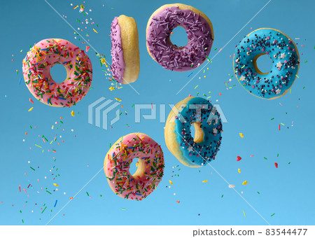 sweet multicolored donuts levitate on a blue background, sugar sprinkles are flying around sweet multicolored donuts levitate on a blue background, sugar sprinkles are flying around 83544477