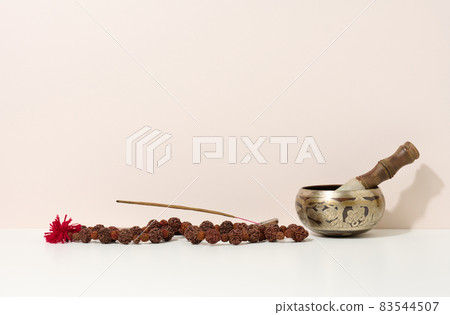 copper singing bowl and wooden clapper on a white table. Musical instrument for meditation, relaxation, various medical practices related to biorhythms, normalization of mental health copper singing bowl and wooden clapper on a white table. Musical instrument for meditation, relaxation, various medical practices related to biorhythms, normalization of mental health 83544507