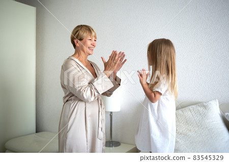 Little girl with grandmother clap their hands in the bedroom on the bed Little girl with grandmother clap their hands in the bedroom on the bed 83545329