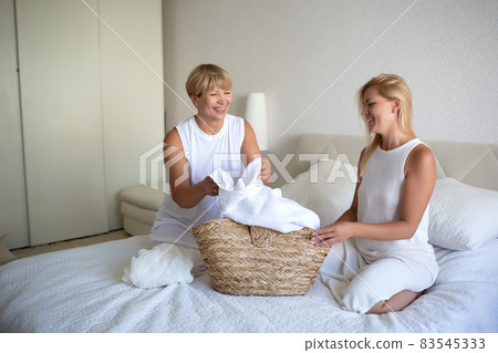 woman with mom disassemble the laundry while sitting on the bed in the bedroom woman with mom disassemble the laundry while sitting on the bed in the bedroom 83545333