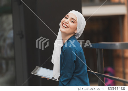 Smiling muslim girl using digital tablet, browsing Internet or social networks outdoor Smiling muslim girl using digital tablet, browsing Internet or social networks outdoor 83545488