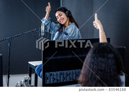 female studio technician of the computer monitor of Software for recording in foreground of young Asian woman vocalist Wearing Headphones recording a song front of microphone in a professional studio female studio technician of the computer monitor of Software for recording in foreground of young Asian woman vocalist Wearing Headphones recording a song front of microphone in a professional studio 83546188