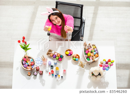 Easter holiday concept,Happy Asian Young woman holding with colorful Easter eggs on white wooden table background in top view 83546260