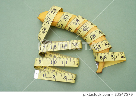 Above view of ripe banana wrapped into tape measure against green background 83547579