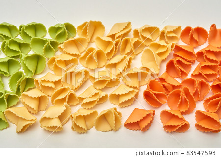 Rows of colorful raw pasta shaped as corners on isolated background, italian food concept Rows of colorful raw pasta shaped as corners on isolated background, italian food concept 83547593