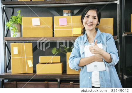 Asian woman startup small business at home office. Online seller entrepreneur young asian woman use tablet checking online order. Woman using tablet check stock goods supply delivery package shipping 83549042