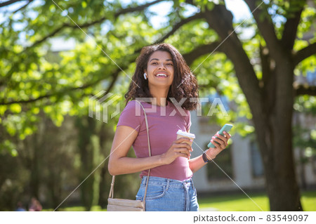 Smiling mulatta with a coffee cup in hands in the park 83549097