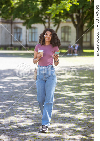 Smiling mulatta with a coffee cup in hands in the park 83549099