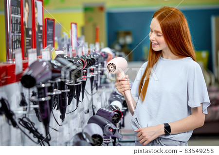 Pleasant woman in electronics store is testing hairdryer, want to buy, focus on hair dryer Pleasant woman in electronics store is testing hairdryer, want to buy, focus on hair dryer 83549258