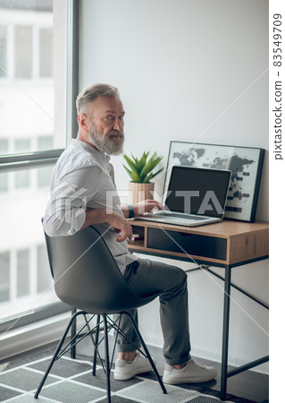 A mature man in white tshirt working on a laptop 83549709