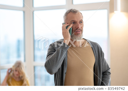 A gray-haired mature man talking on the phone and looking pleased A gray-haired mature man talking on the phone and looking pleased 83549742
