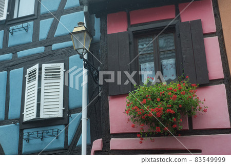 Closeup of medieval house facade with red geranium at the window in the famous village of Bergheim in France 83549999