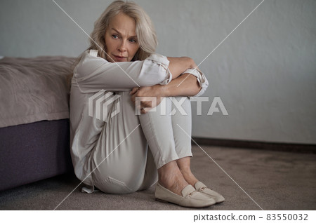 Beautiful low-spirited lady seated on the carpet looking away 83550032