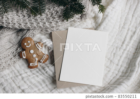 Christmas still life. Blank greeting card, invitation mockup with craft envelope.,Gingerbread man cookie and fir tree branches. White muslin table cloth, throw. Flatlay, top view. Winter holiday. 83550211