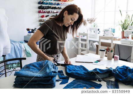 Denim Upcycling Ideas, Using Old Jeans, Repurposing Jeans, Reusing Old Jeans, Upcycle Stuff. Woman seamstress cut and repair old blue jeans in sewing studio. Denim Upcycling Ideas, Using Old Jeans, Repurposing Jeans, Reusing Old Jeans, Upcycle Stuff. Woman seamstress cut and repair old blue jeans in sewing studio. 83550949