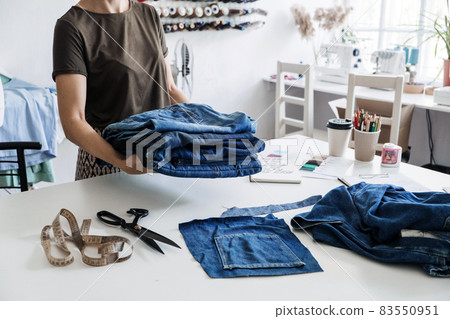Denim Upcycling Ideas, Using Old Jeans, Repurposing Jeans, Reusing Old Jeans, Upcycle Stuff. Woman seamstress holding Stack of old blue jeans in sewing studio. Denim Upcycling Ideas, Using Old Jeans, Repurposing Jeans, Reusing Old Jeans, Upcycle Stuff. Woman seamstress holding Stack of old blue jeans in sewing studio. 83550951