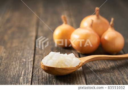 Chopped onion in a wooden spoon on a rustic table, copy space for text. 83551032