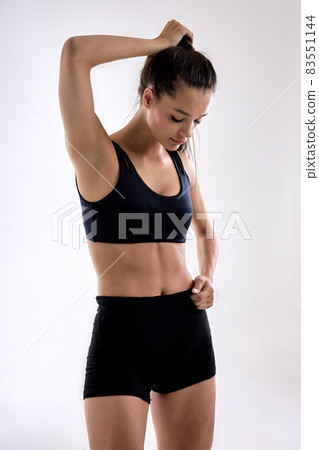 Amusing fintess lady in black top holding long hair in ponytail over white background 83551144