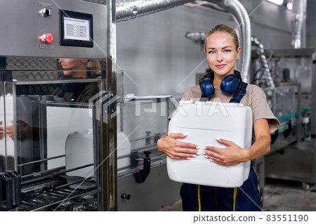 woman worker in factory next to robotic equipment holding canister bottle 83551190
