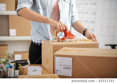 Close-up of unrecognizable woman standing at table with packages and taping parcel box before delivery 83551191