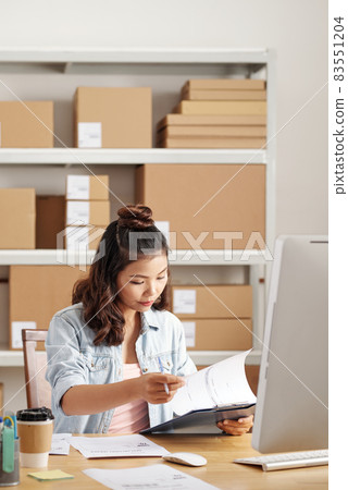 Concentrated Asian manager sitting at desk with computer and analyzing business papers in office 83551204