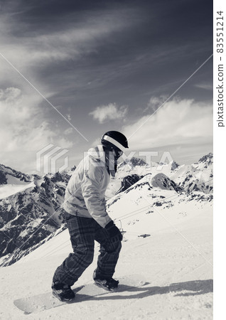 Snowboarder downhill on snowy ski slope in high mountains. Black and white retro toned image. 83551214