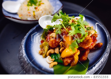 A dish with barbecue sauce and cashews on a blue round plate, garnished with herbs. A dish with barbecue sauce and cashews on a blue round plate, garnished with herbs. 83551333