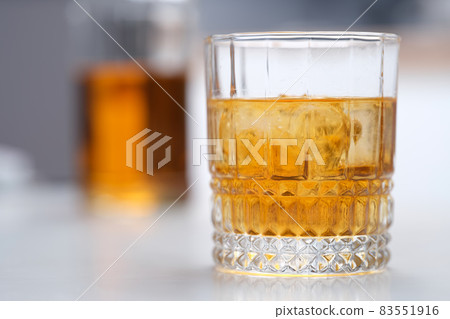 Glass of whiskey with ice standing on table closeup Glass of whiskey with ice standing on table closeup 83551916
