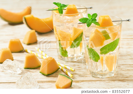 Melon lemonade with ice and mint in a glass on a wooden table. Melon water in glass jars. 83552077
