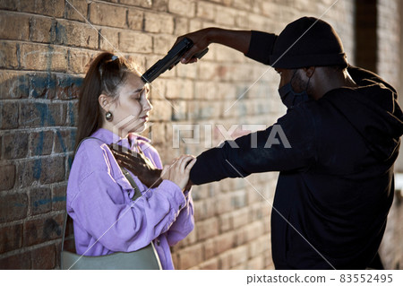 Rape victim sad and scared female is leaned on wall, gun-threatened by maniac in dark tunnel Rape victim sad and scared female is leaned on wall, gun-threatened by maniac in dark tunnel 83552495