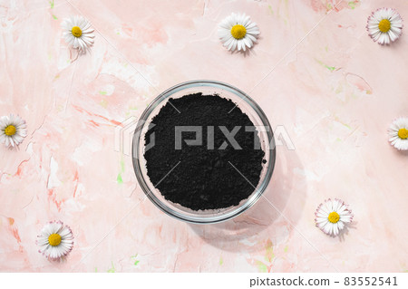 Black activated charcoal powder in a glass bowl on pastel pink floral background. Ingredient for beauty, cosmetics, spa treatment, detox concept. Top view, copy space 83552541
