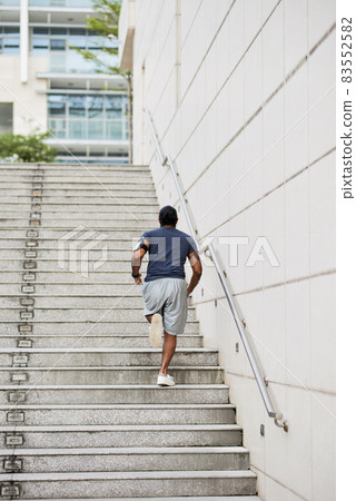 Rear view of sporty man with phone arm band running up stairs while practicing stair workout in city 83552582