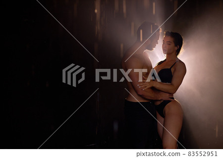 Temptive sensual couple posing in dark studio room, light and rain in the background 83552951